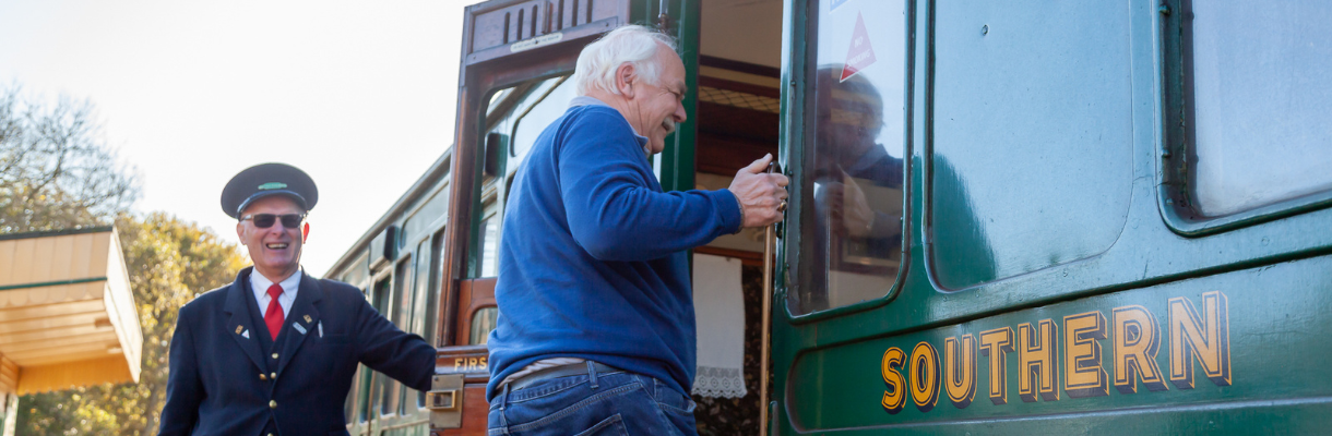 Conductor holding the door for a man stepping on the Isle of Wight Steam Railway train